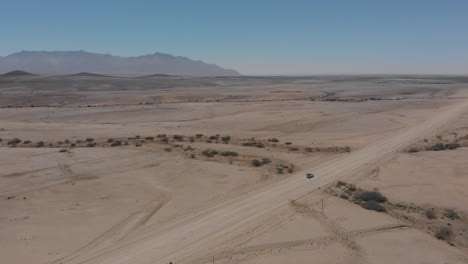 Single-vehicle-driving-on-empty-gravel-road-in-desert