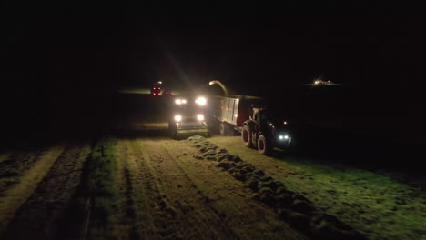 Pull-back-aerial-shot-of-chopper-feeder---grass-tractor-working-by-spotlight-at-night