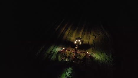 Aerial-view-overhead-farming-vehicle-working-by-spot-light-at-night