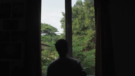 Long-shot-of-silhouette-of-a-photographer-taking-photos-of-something-outside-the-window,-with-trees-on-the-background
