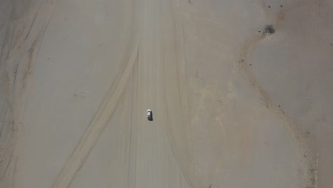 Top-down-aerial-shot-of-single-vehicle-travelling-on-empty-deserted-gravel-road
