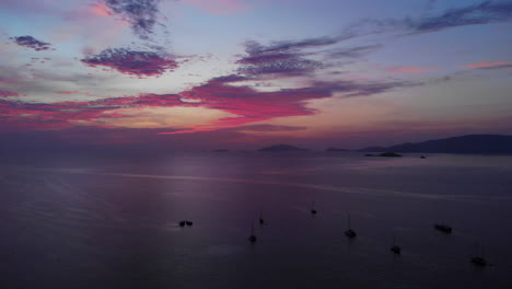 Luftaufnahme-Eines-Farbenfrohen-Sonnenuntergangs-über-Dem-Ozean-Mit-Booten-Und-Bergen-Im-Hintergrund