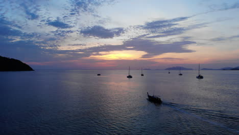 Ein-Thailändisches-Geschichtenboot,-Das-Mit-Anderen-Verankerten-Booten-Dem-Sonnenuntergang-Entgegen-Segelt