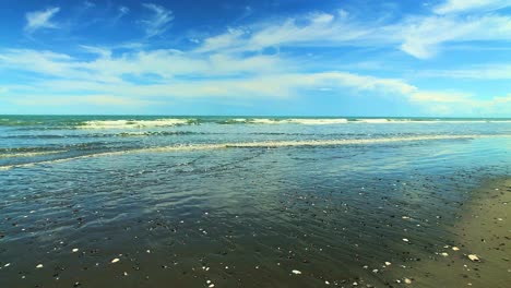 Slow-pan-left-of-Gentle-waves-on-Otaki-Beach,-New-Zealand-on-a-Beautiful-Sunny-day