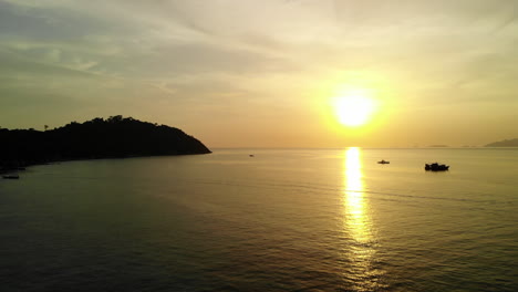Friedlicher-Ozean-Mit-Einem-Goldenen-Sonnenuntergang,-Booten-Und-Bergen-Im-Hintergrund