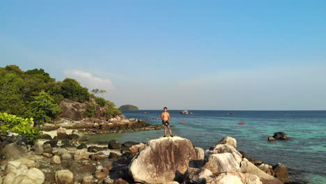 Aerial-footage-of-a-small-island-flying-away-a-white-shirtless-man-on-top-of-rocks