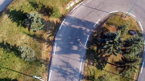 drone-footage-from-above-of-a-man-skateboarding-down-a-hill-on-a-very-bendy-road-with-lots-of-turns,-filmed-in-the-evening-with-a-golden-glow-to-the-picture