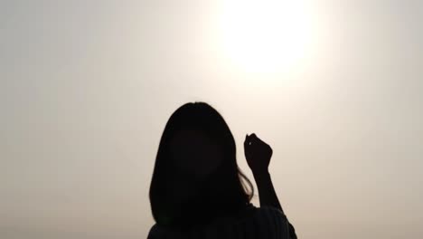 Silhouette-of-an-asian-girl-raising-her-hand-towards-the-sun,-clenching-her-fist-and-put-her-hand-down