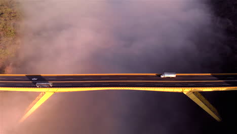 AERIAL:-REVEAL-SHOT-OF-A-BRIDGE-WITH-FOG-IN-SUNSET