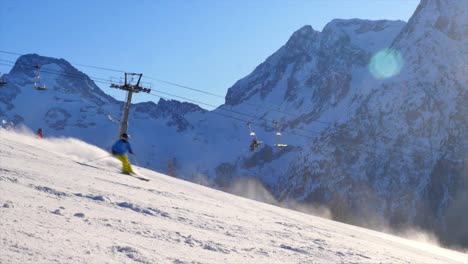 unrecognizable-single-skier-going-down-a-steep-black-piste-praying-snow-with-beautiful-mountain-background-on-a-sunny-day-with-blue-skies