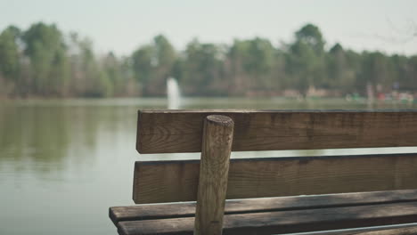 Left-side-of-a-wooden-bench-in-front-of-a-lake-with-a-water-fountain-in-the-middle