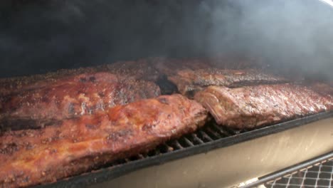 Close-up-of-smoke-blowing-over-racks-of-ribs-in-an-off-set-smoker