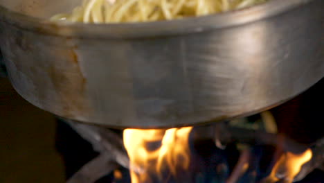 A-close-up-of-pasta-and-veggies-being-cooked-in-a-pan-over-fire-in-slow-motion