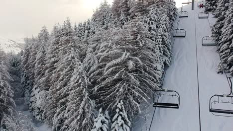 Drohnen-Rundblick-Aus-Der-Luft-Auf-Den-Skilift,-Der-Zwischen-Hohen-Schneebedeckten-Bäumen-In-Den-Französischen-Alpen-Vorbeifährt