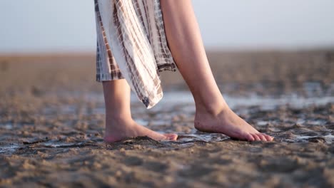 Low-angle-and-closeup-of-a-girl's-feet-standing-on-a-wet-sand-at-a-beach-near-the-sea