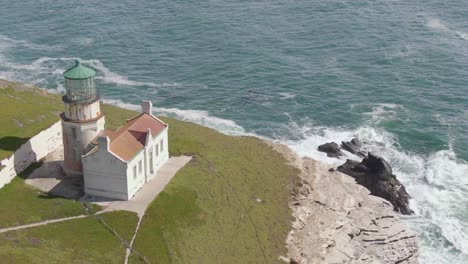 Historic-lighthouse-on-coastal-cliffs,-push-in-drone-shot-with-tilt