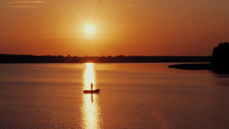 Aerial-shot-of-men-fishing-from-the-boat-in-front-of-shiny-sun-at-evening