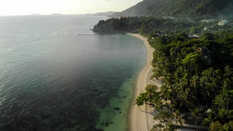 Crane-shot-by-drone-of-a-beautiful-beach-in-Thailand,-with-a-mist-over-the-trees