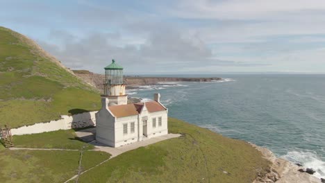 Historic-lighthouse-on-coastal-cliff-side,-push-in-drone-shot