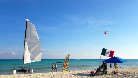 Boat-And-Water-Sports-Stand-On-The-Beach-With-People-Walking-By-In-Bathing-Suits-In-Playa-Del-Carmen-Mexico