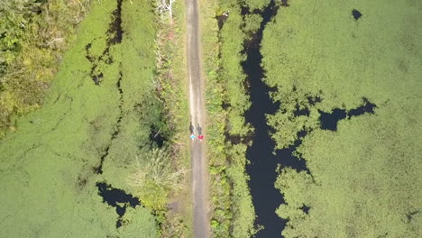 pull-back-drone-clip-of-two-runners-on-a-narrow-path-in-the-middle-of-a-pond
