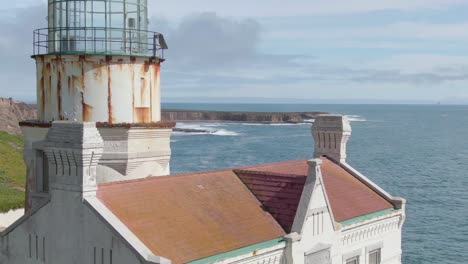 Historic-lighthouse-on-California-coastal-cliffs,-aerial-close-orbit