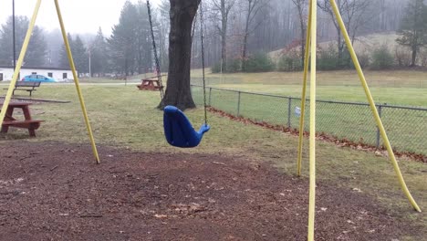 Deserted-playground-swings-swinging-empty-and-lonely-on-a-rainy-and-dreary-day-with-motion