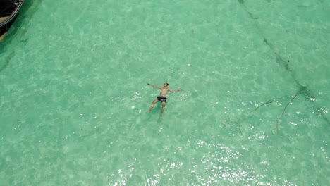 Man-floating-and-resting-in-clear-ocean-water-near-a-boat