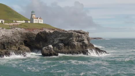 Historic-lighthouse-on-coastal-cliffs,-low-drone-orbit