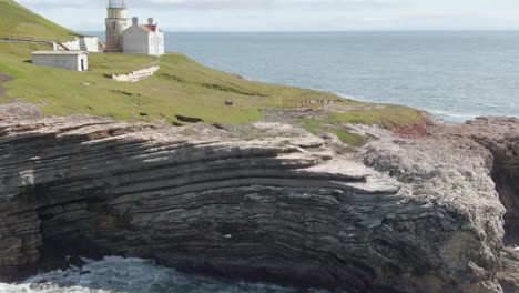 Historic-lighthouse-on-coastal-cliffs,-drone-descent-with-tilt