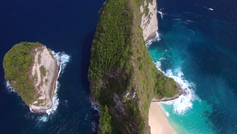 drone-flying-close-forward-tilt-down-above-kelingking-beach-on-nusa-penida-island-over-the-seashore-green-peninsula-cliff-ridge