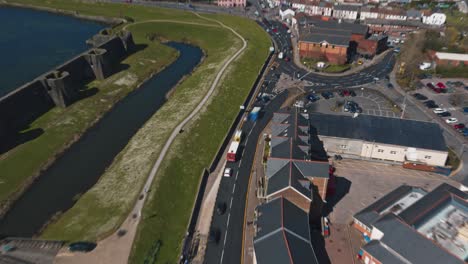 Reverse-hyperlapse-aerial-drone-shot-of-road-traffic-through-town-revealing-Caerphiilly-Castle-during-busy-Spring-morning-in-April-with-blue-skies