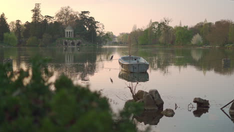 A-static-shot-of-an-abandoned-boat-in-the-middle-of-the-lake-of-the-Vincennes-Woods-Parc-at-sunset-in-Paris,-France