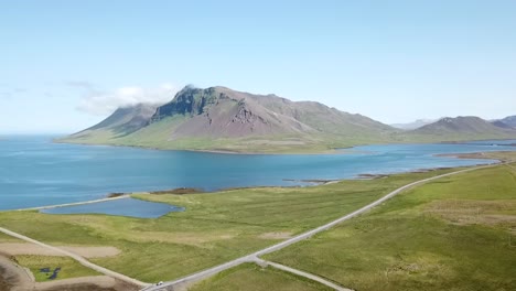 Una-Trayectoria-De-Vuelo-Recta-Tomada-De-Una-Gran-Montaña-Verde-Vibrante-Rodeada-Por-Un-Lago-En-Islandia