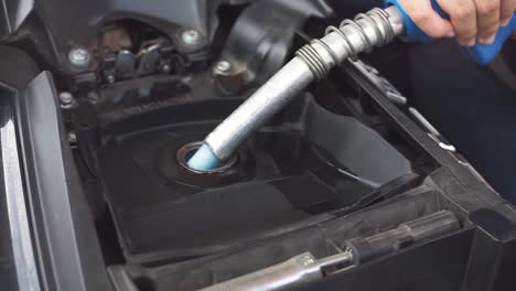 Closeup-of-hand-handling-fuel-nozzle-ejecting-benzine-to-motorcycle-or-scooter-fuel-chamber