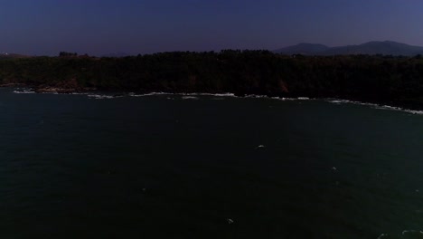 drone-footage-moving-from-open-sea-towards-a-rocky-beach-with-waves-crashing