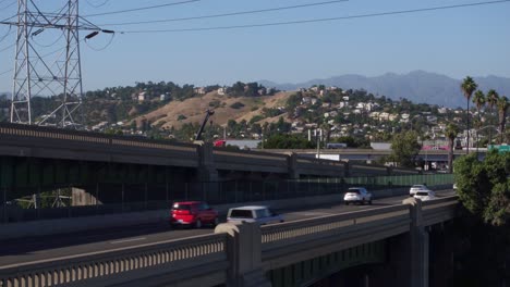 Drohnenaufnahme-Des-Verkehrs-In-Los-Angeles-Auf-Einer-Brücke-Mit-Ikonischen-Palmen-Im-Hintergrund