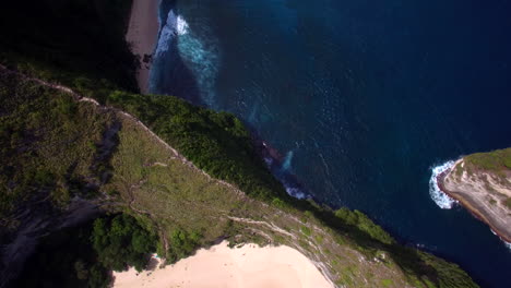 drone-flying-close-forward-close-above-kelingking-beach-on-nusa-penida-island-green-peninsula-cliff-ridge