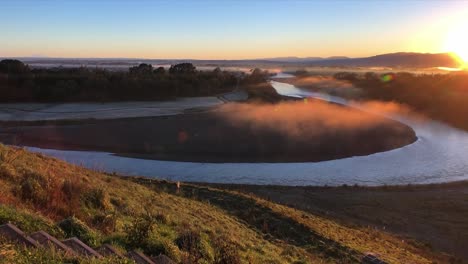 Langsamer-Zoom-Eines-Blicks-über-Einen-Nebligen-Neuseeländischen-Fluss-Mit-Dem-Goldenen-Schein-Der-Aufgehenden-Sonne