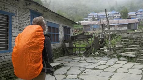 Zeitlupe-Junger-Mann,-Der-Mit-Einem-Orangefarbenen-Rucksack-Durch-Das-Dorf-In-Nepal-Wandert