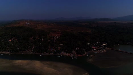 Drone-moving-forwards-a-fishing-village-set-on-a-back-water-with-rolling-hills-with-a-temple-and-a-light-house