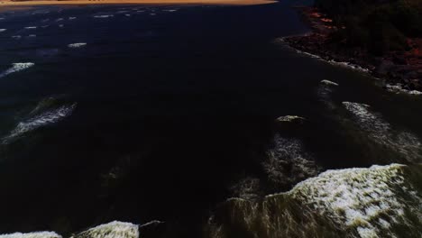 Drone-footage-following-the-waves-crashing-on-to-a-rocky-beach,-shot-in-South-GOA