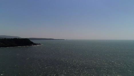 Drone-footage-moving-along-open-sea-with-mountains-on-the-shore-looking-at-the-horizon