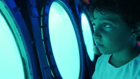 A-young-boy-looks-out-the-round-windows-of-a-submarine-with-wonder-in-his-eyes