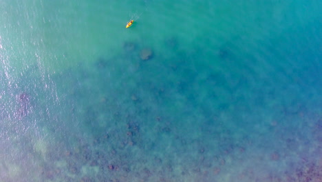spinning-drone-shot-of-the-yellow-kayak-above-the-sea-next-to-the-pink-beach,-travel-destination,-outdoor-scene,-couple-paddling-in-the-boat