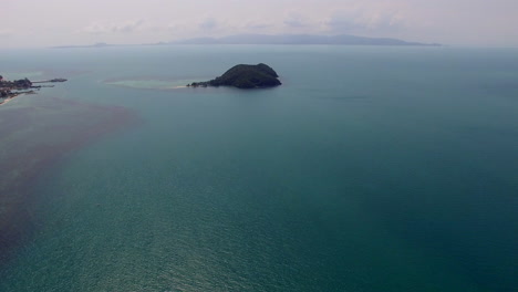 drone-slowly-flying-forward-approaching-to-the-tiny-tropical-island-in-Thailand-above-the-bay-turquoise-calm-water,-sea-landscape,-vocation-destination-paradise,-sunny-and-cloudy