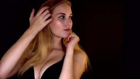 Portrait-of-beautiful-blonde-with-long-hair-in-a-bra-touching-face-with-clean-and-healthy-skin-on-a-black-studio-background