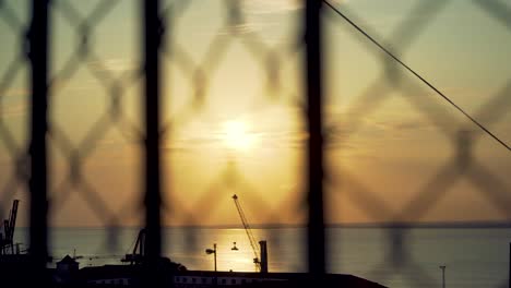 Lisbon-harbor-sunrise-with-cranes-silhouette-through-out-of-focus-wire-fences