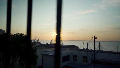 Lisbon-harbor-sunrise-with-cranes-silhouette-through-rusty-fences