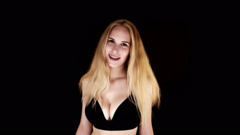 Beautiful-young-woman-with-big-natural-breasts-in-a-black-bra-on-a-black-background-laughing-at-the-camera